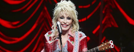 Dolly Parton holding a guitar and standing in front of a microphone on a stage