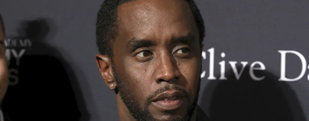Sean Combs in a patterned blazer and silver chains posing against a dark backdrop. Sean Combs in a patterned blazer and silver chains posing against a dark backdrop.