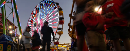 People walk toward or away from a lighted Ferris wheel.