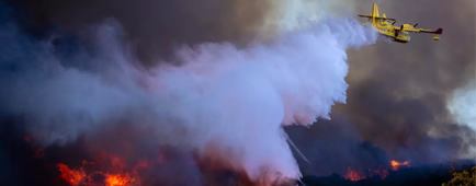 An airplane dumps water over a canyon fire.