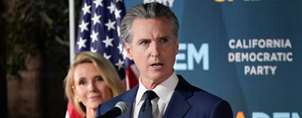 A man in dark suit and tie gestures while speaking, as a woman with blond hair looks on A man in dark suit and tie gestures while speaking, as a woman with blond hair looks on