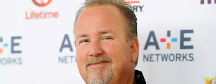 "Storage Wars" cast member Darrell Sheets  wears a black collared shirt and smiles toward a camera.