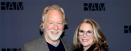 Timothy Busfield, in a suit jacket, and Melissa Gilbert, in black jacket, glasses and dangly earrings, smile for a photo.