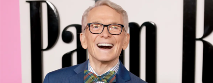 Bob Mackie wears a blue suit and bow tie and smiles. 