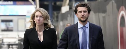 Elizabeth Holmes and Billy Evans, both wearing suits, walk hand in hand.