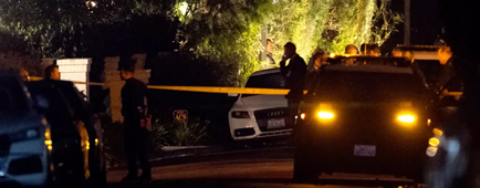 A few people stand near a yellow tape spread across a driveway. A few people stand near a yellow tape spread across a driveway.