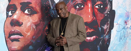 A person poses in front of a mural.