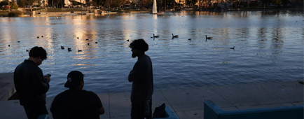 three people converse near a lake at MacArthur Park at sunset.