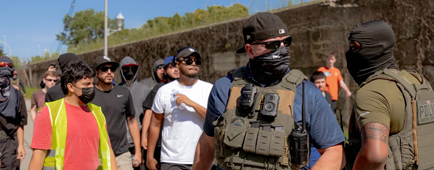 Masked agents in vests standing near other people