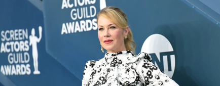 Christina Applegate poses against a dark blue backdrop in a white-and-black patterned dress.